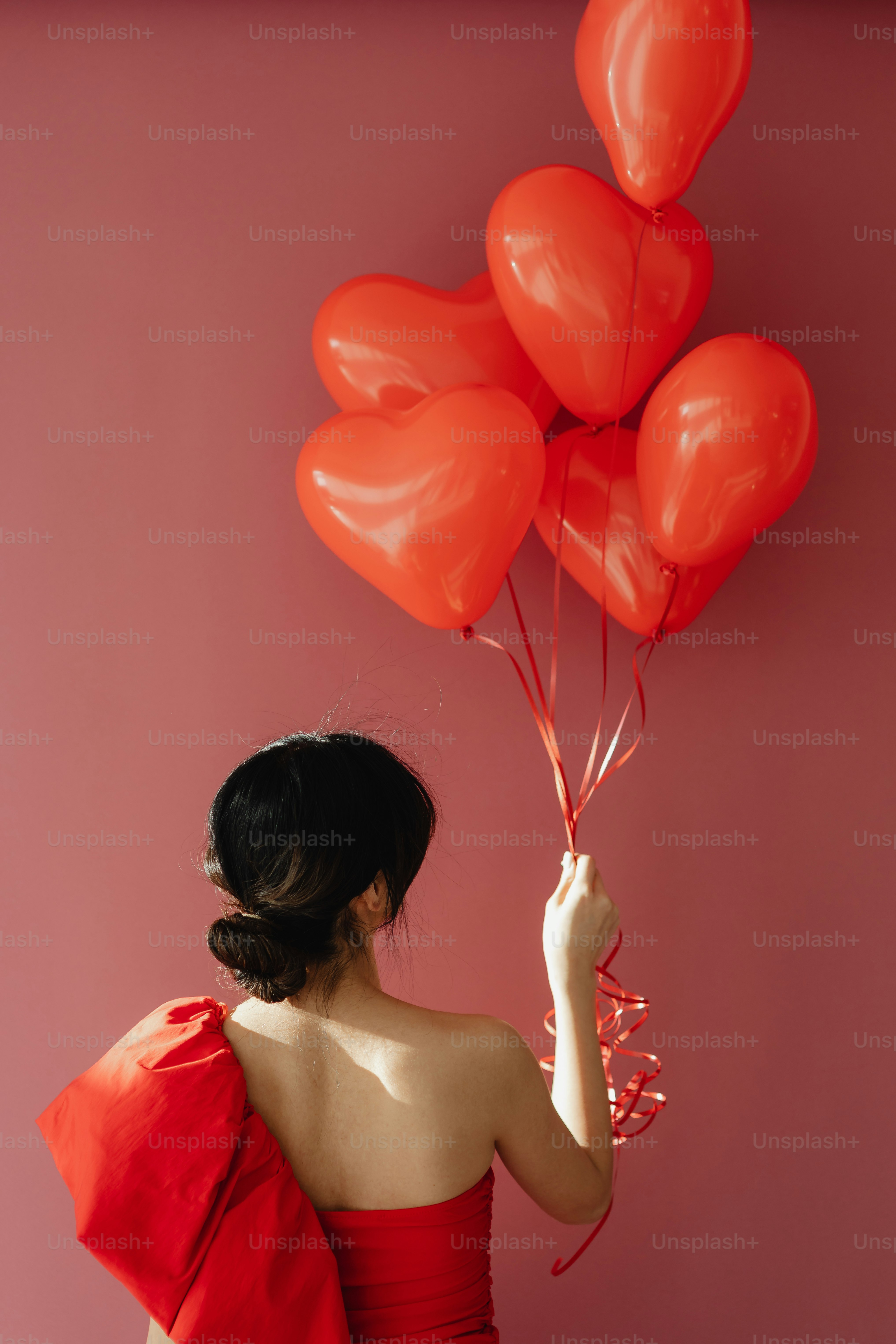 a woman in a red dress holding a bunch of red heart shaped balloons